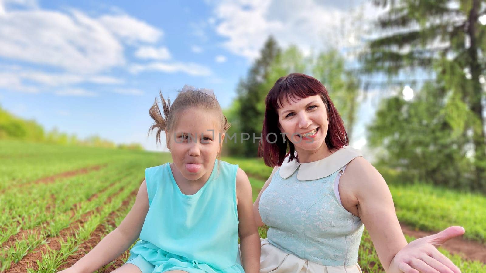 Happy mother and daughter enjoying rest, playing and fun on nature in green field. Woman and girl resting outdoors in summer or spring day