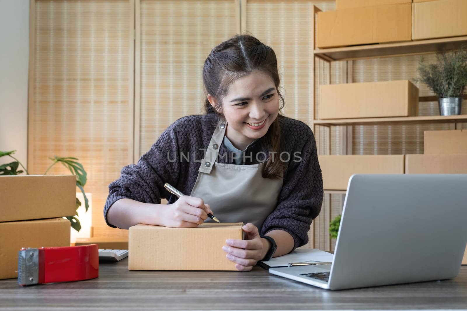 SME business entrepreneurs small in Asia Write shipping information on a cardboard box in home office. Small business operators preparing to ship to customer.