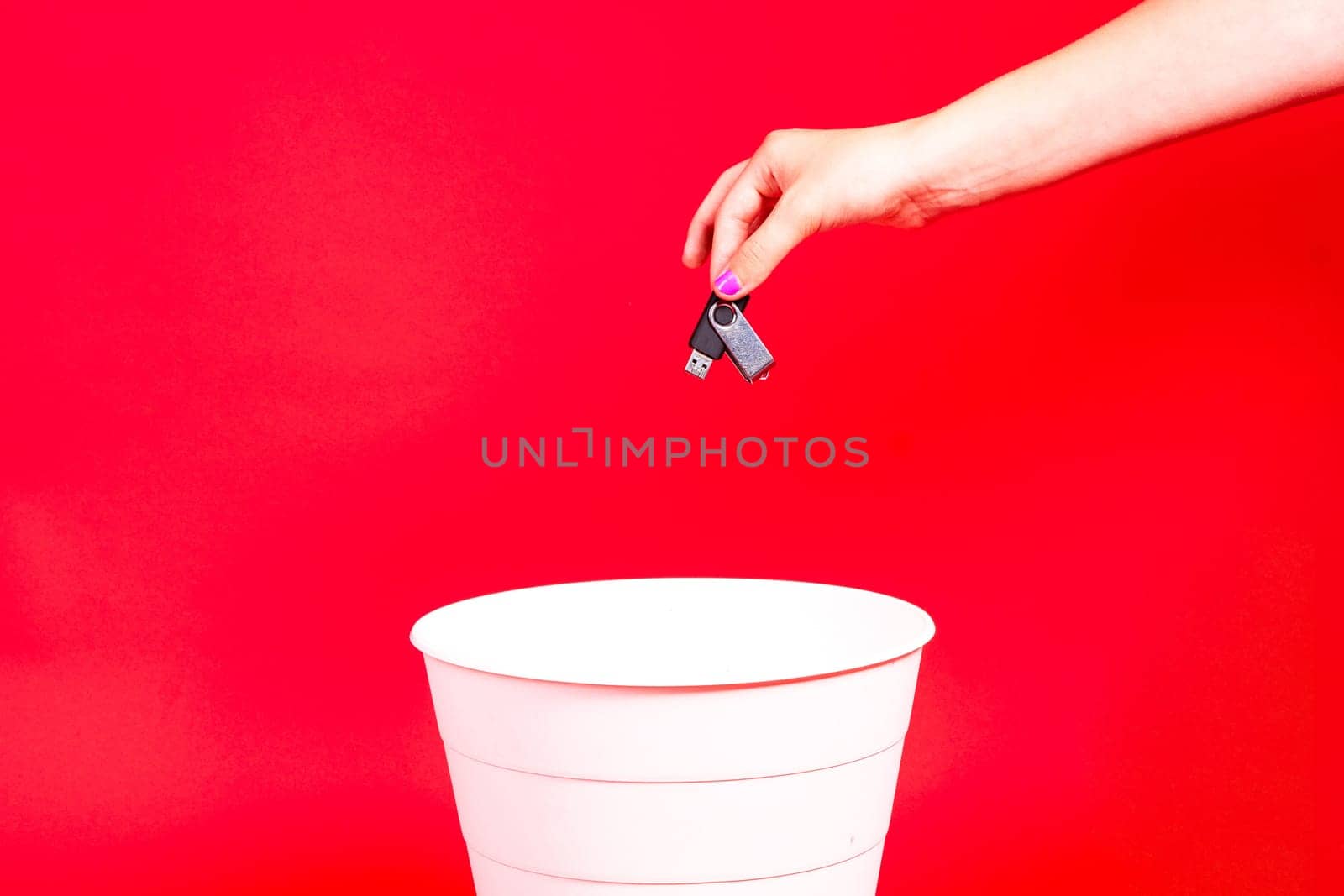 Metal flash drive in a hand in trash can on red background. by Zelenin