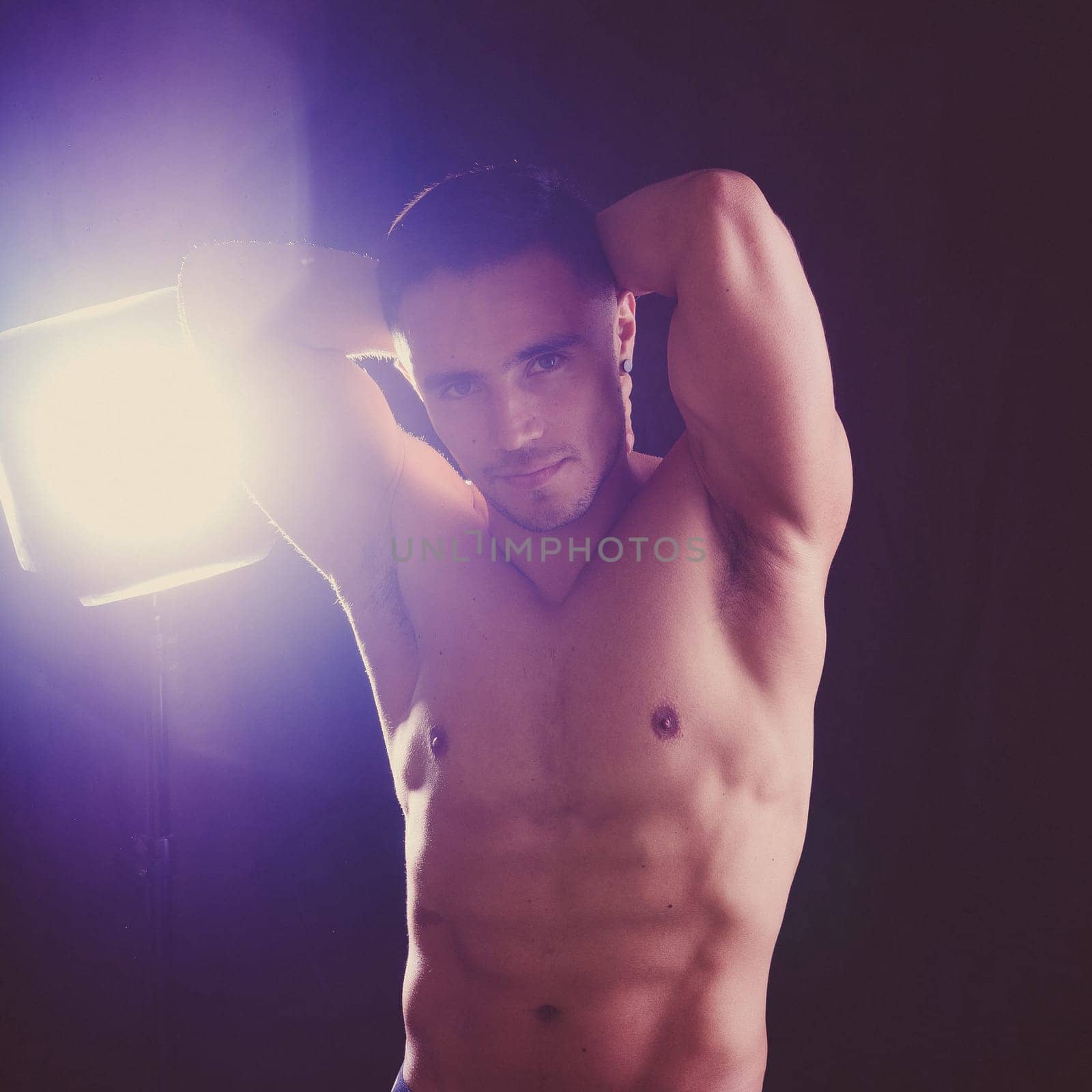 Confident, attractive shirtless muscular young man topless in a studio