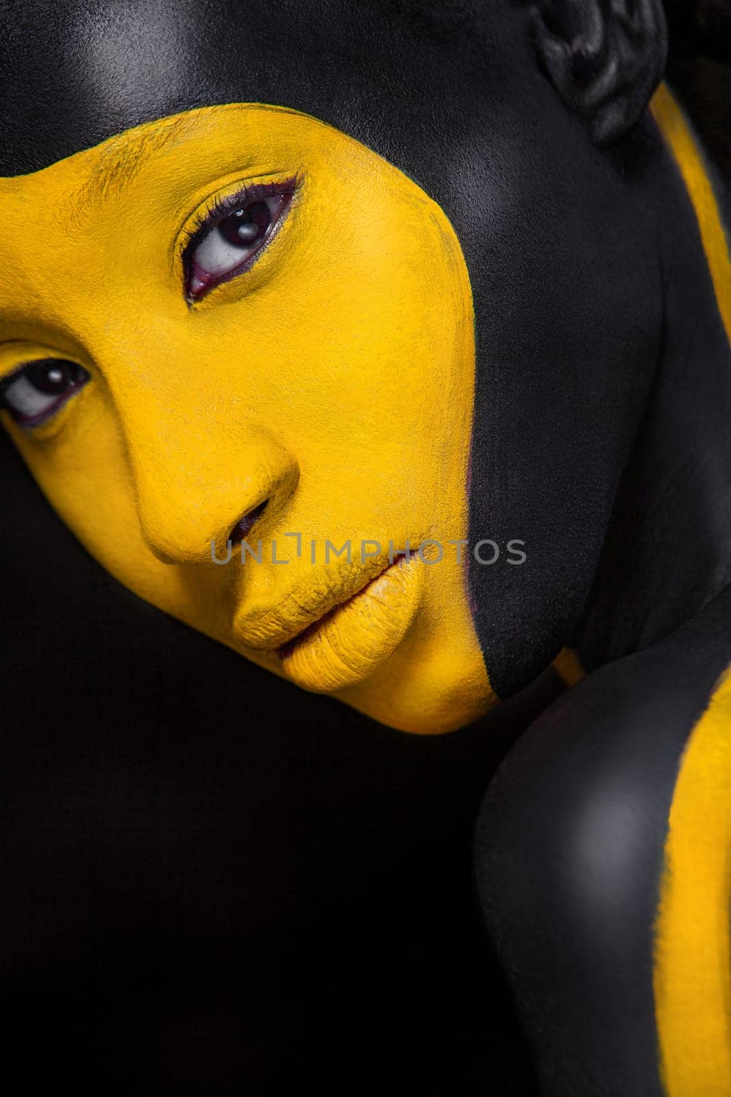 Woman with black body paint. Cheerful young african girl with art bodypaint. An amazing model with yellow makeup. Closeup face.