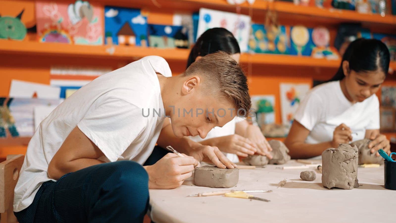 Teenager using carving tool working at clay at pottery workshop. Edification. by biancoblue