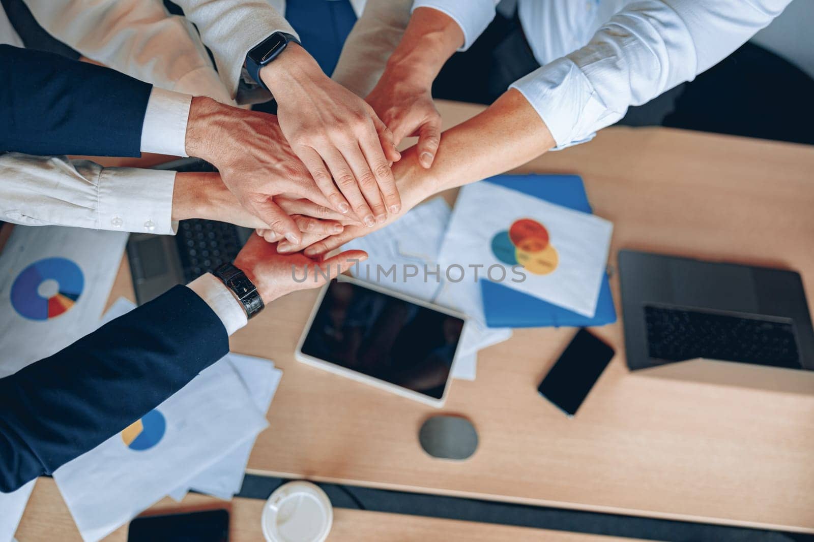 Happy business team celebrating victory in modern office putting their hands together. Top view