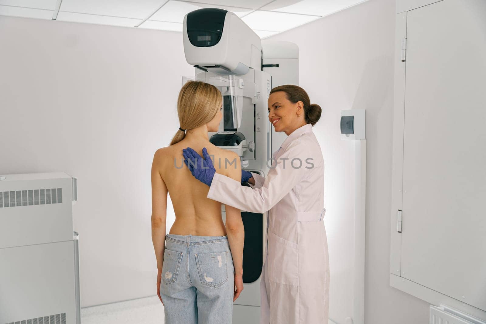Smiling doctor prepairing woman before doing mammogram x-ray to check for breast cancer at hospital by Yaroslav_astakhov