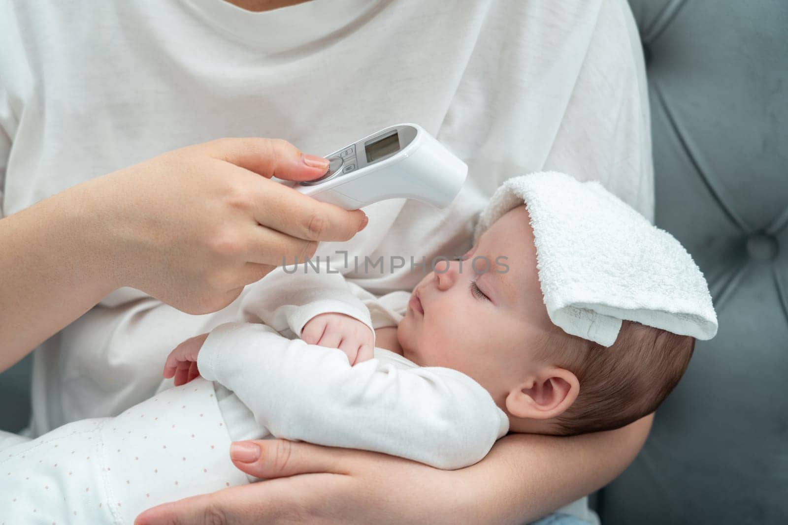 A woman adeptly measures her baby's forehead temperature, utilizing an electronic thermometer for