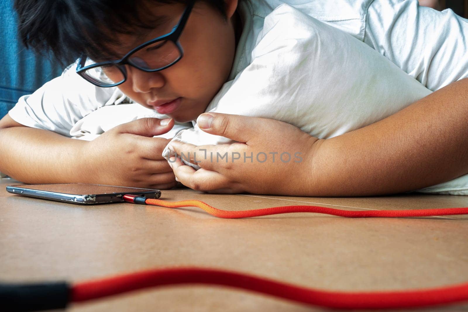 An Asian boy lies prone while seeing media on a smartphone