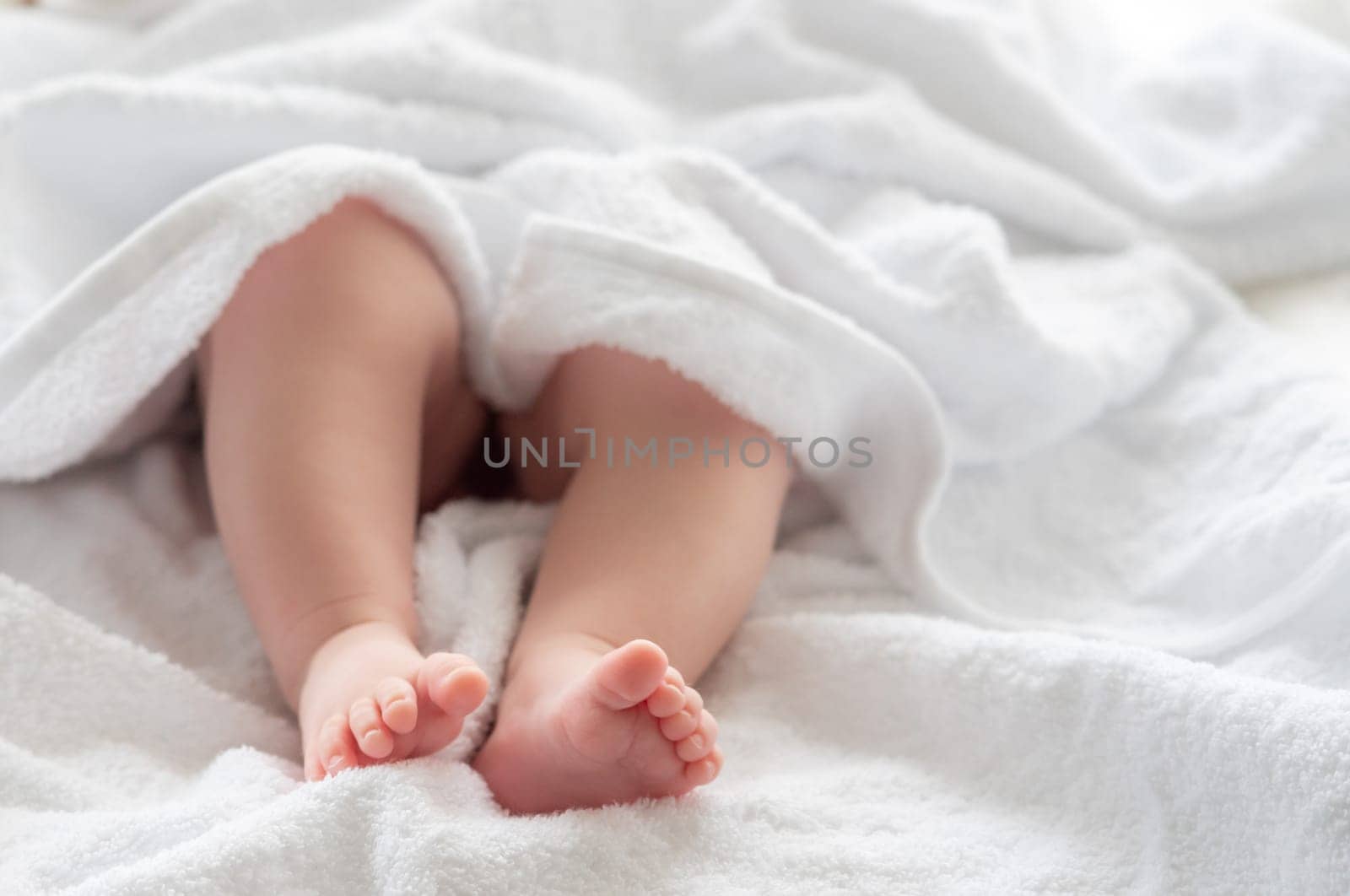 Infant child's tiny feet and legs appearing beneath the gentle cover of a soft white towel, showcasing post-bath serenity