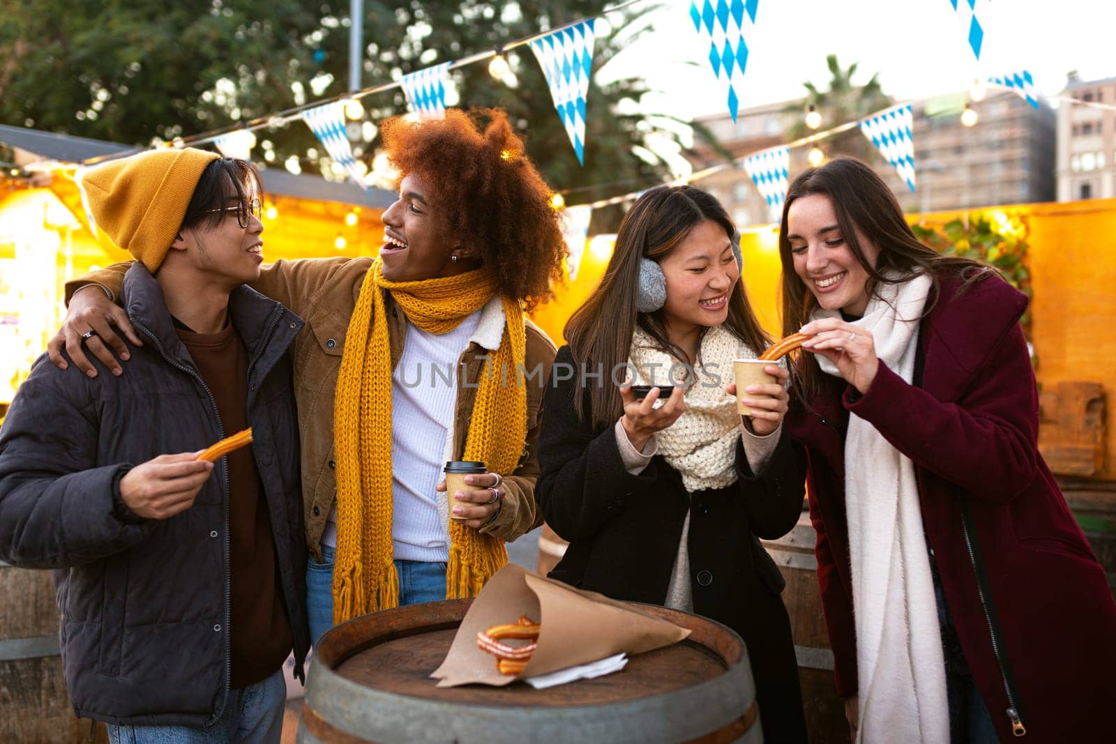 Multiracial friends drinking hot chocolate and eating churros at a winter market. Friendship concept.