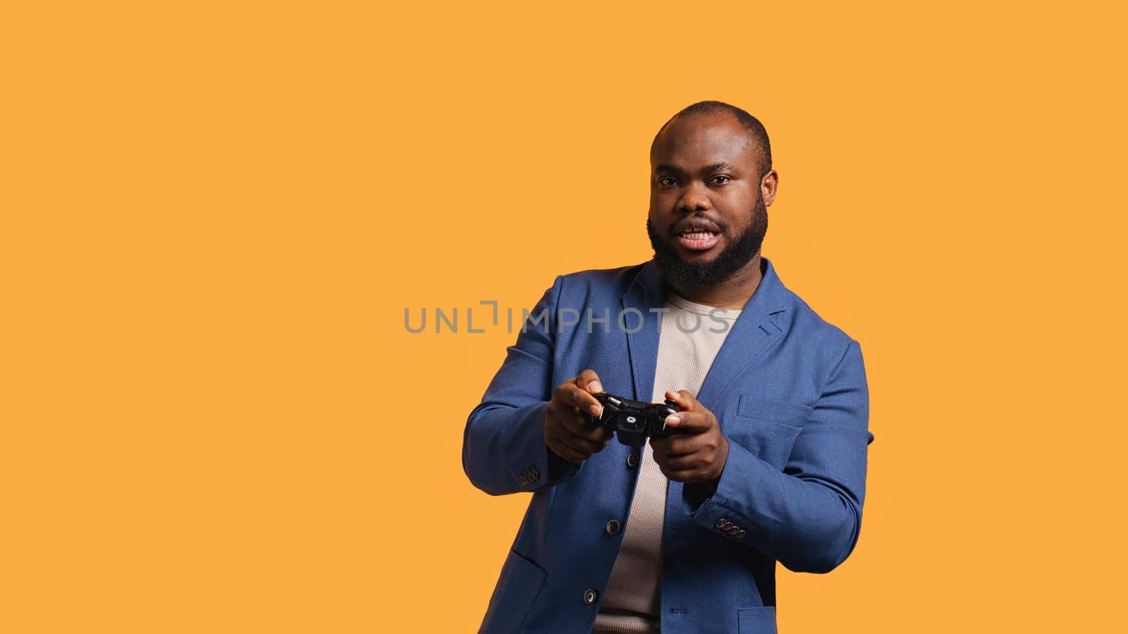 Upset man showing thumbs down sign gesturing holding controller, disapproving of videogames. Displeased BIPOC person against gaming, doing rejection hand gesture, studio background, camera B