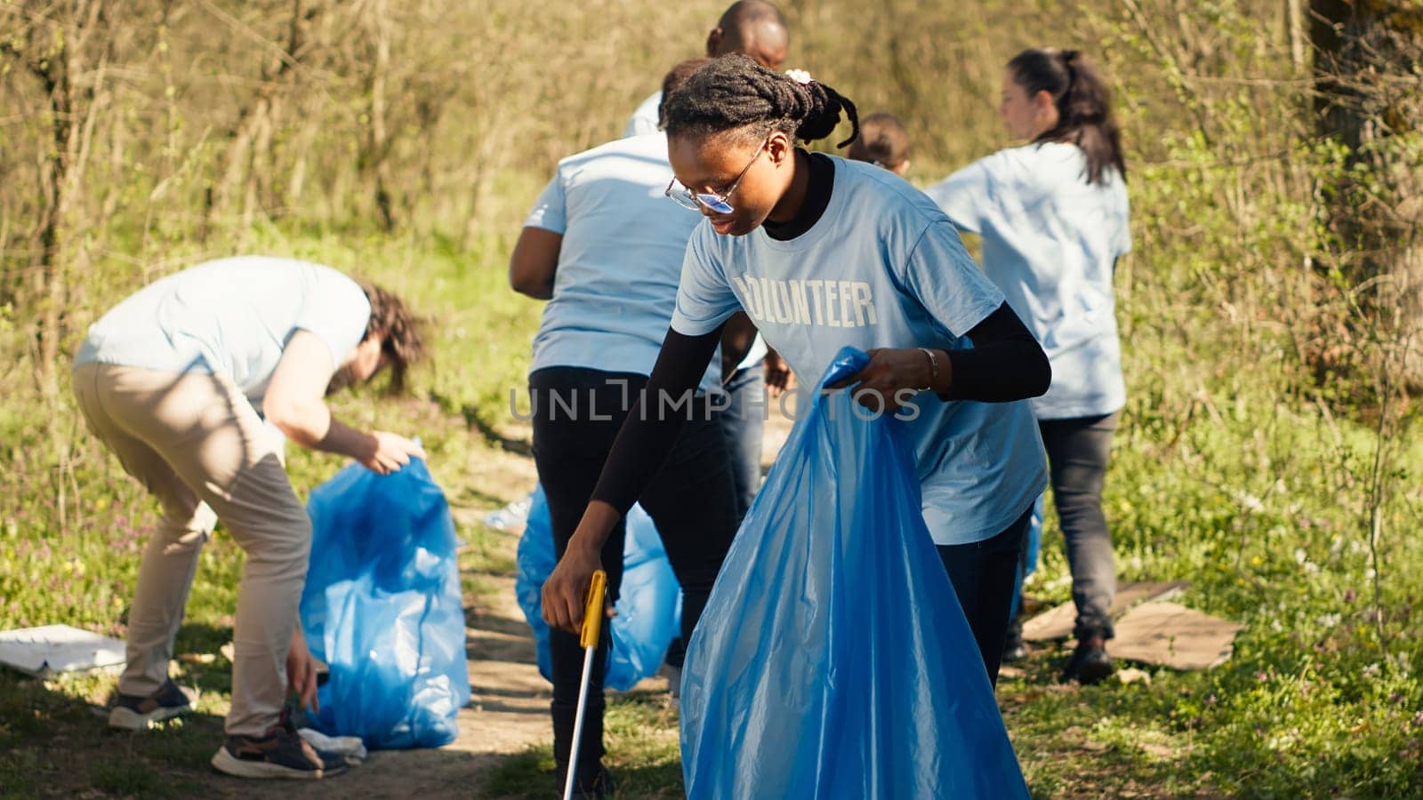 African american girl picking up trash with a long claw and garbage bags by DCStudio