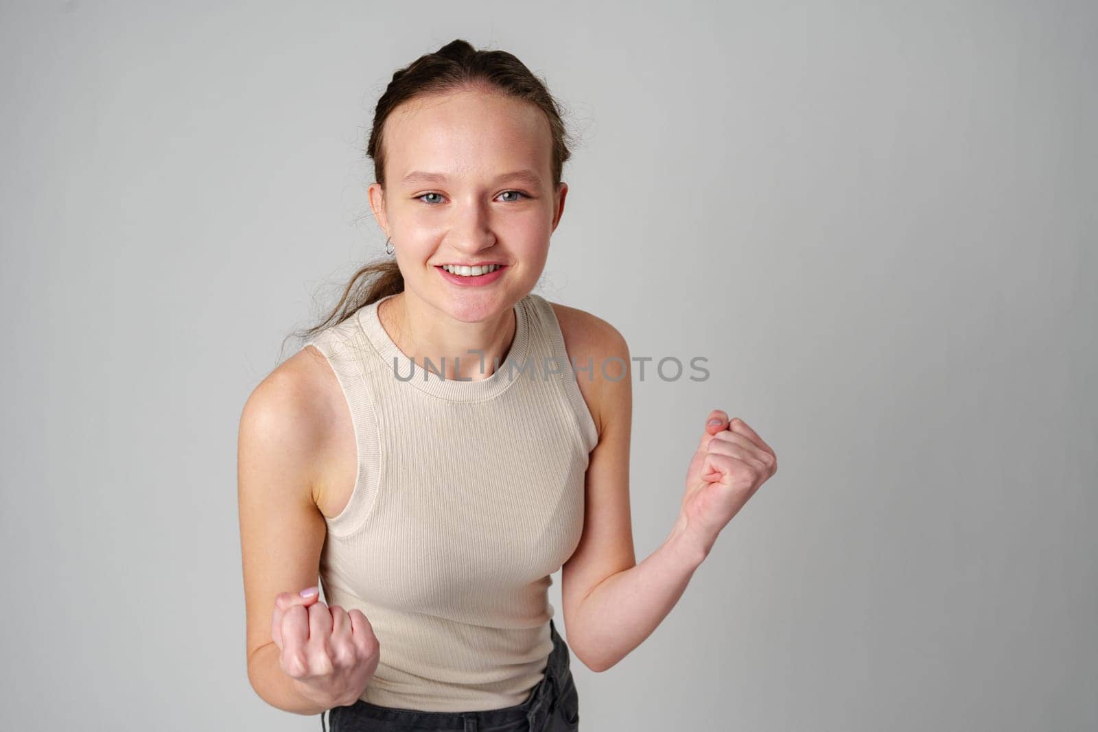 Young Woman in Casual Attire Smiling and Making a Fist Pump Gesture on a Plain Background close up