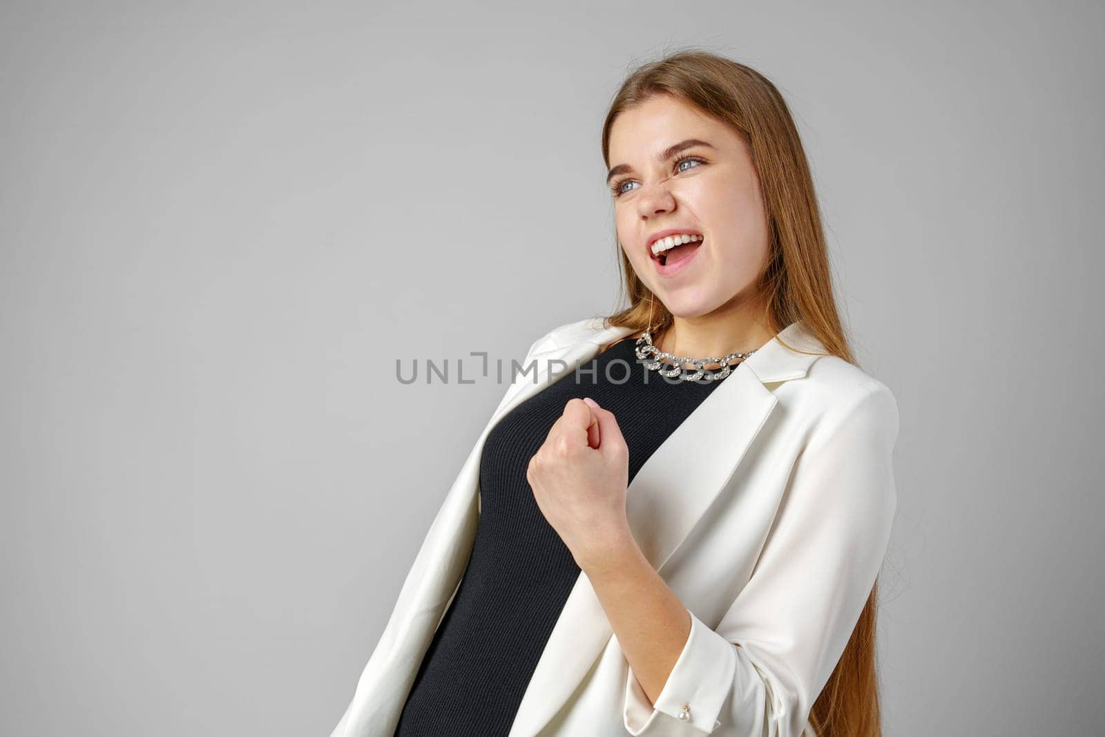 Confident Young Businesswoman Flexing Muscles in Smart Casual Attire Against Grey Background close up