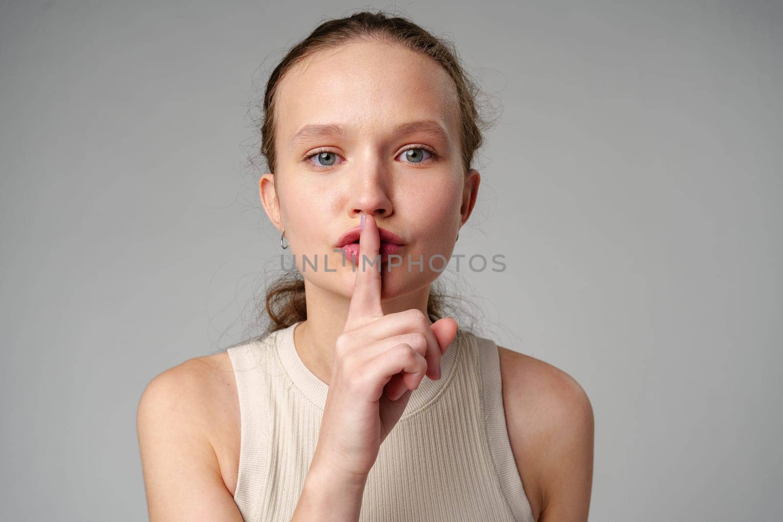 Young Woman Making a Hush Gesture on gray background in studio by Fabrikasimf