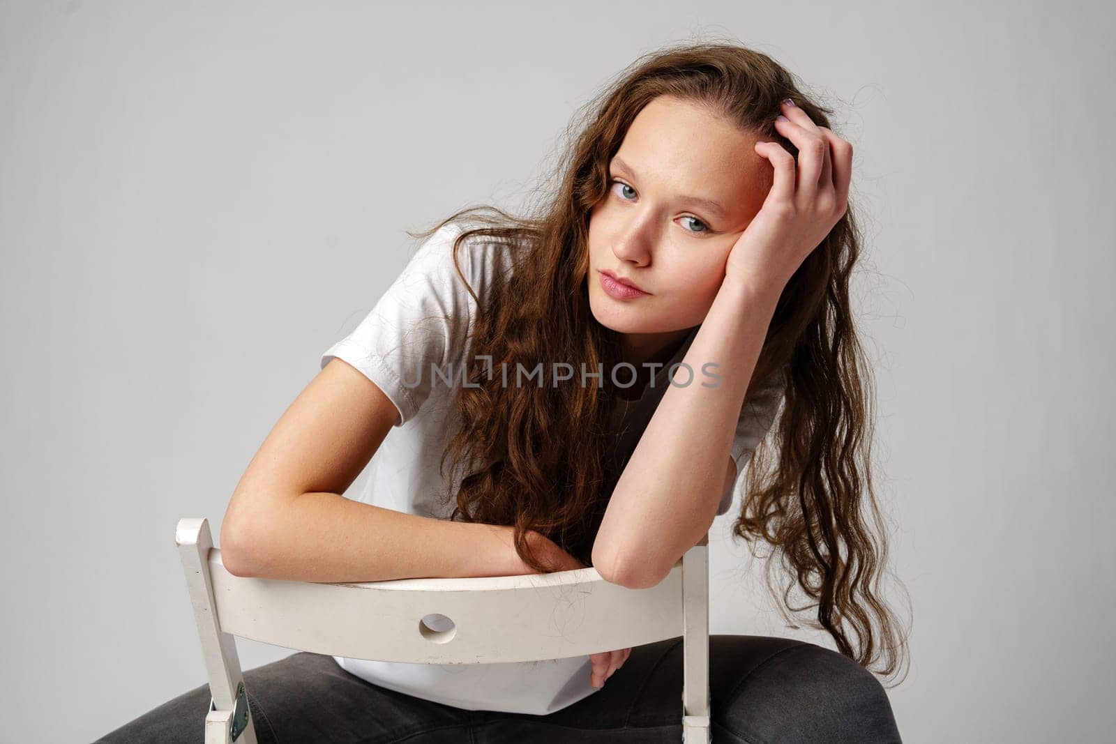 Curly girl model posing on a chair against gray background by Fabrikasimf