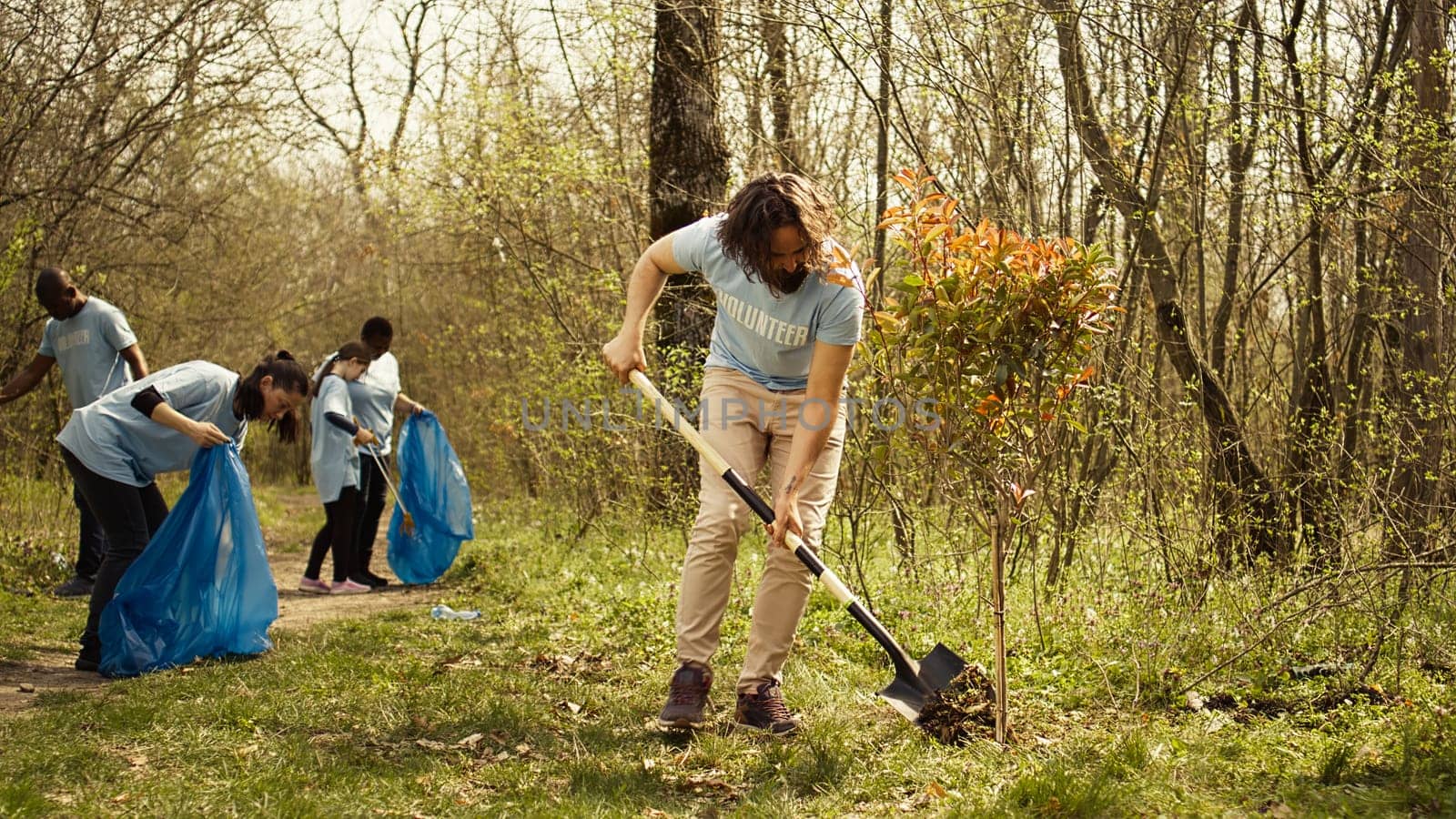 Young man covering base and hole after planting small tree in the woods by DCStudio