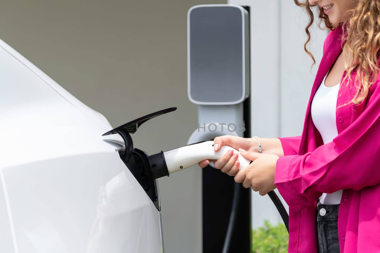 Modern eco-friendly woman recharging electric vehicle from home EV charging station. EV car technology utilized for home resident to future environmental sustainability. Synchronos