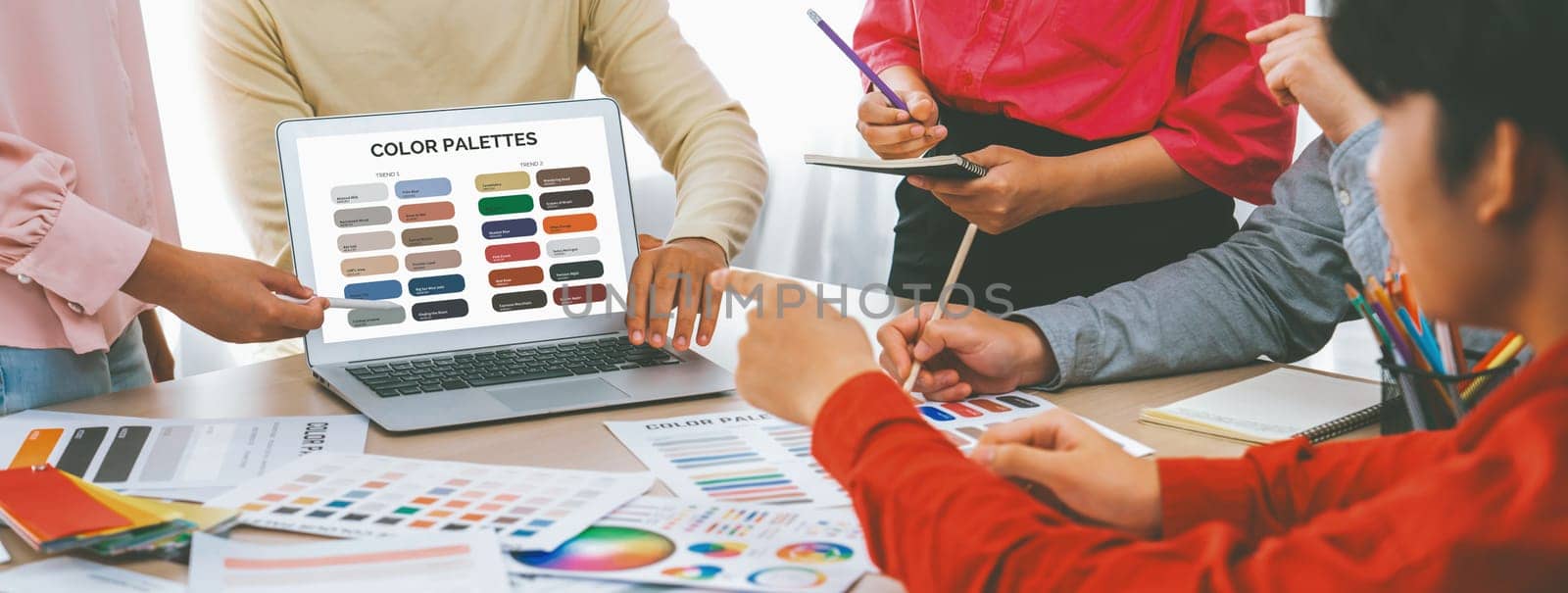 A portrait of creativity graphic designer team select appropriate color for the project by using laptop on table with equipment and designing tool scatter around at modern office. Closeup. Variegated.