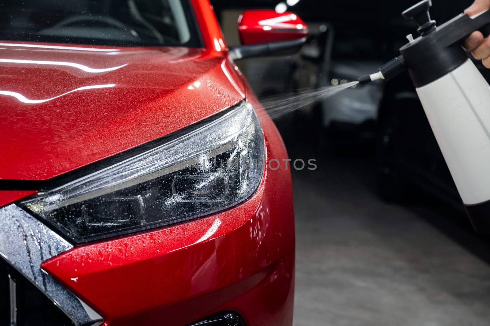 A man washes the headlights of a red car with a spray