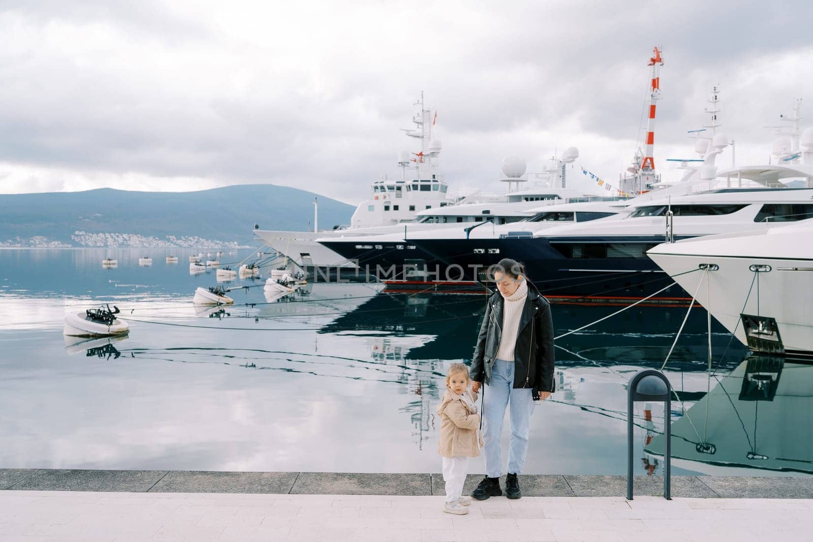 Mom and little girl stand on the embankment next to the moored ships. High quality photo