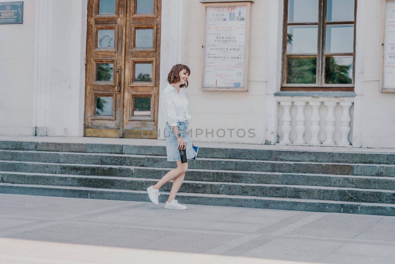 Woman staircase city. A business woman in a white shirt and denim skirt walks down the steps of an ancient building in the city.