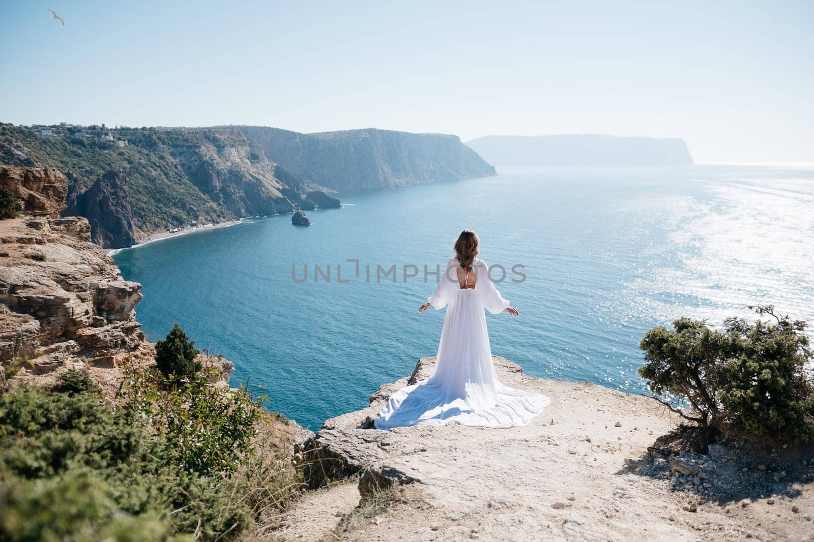 woman stands cliff overlooking the ocean. The sky is clear and the water is calm. The woman is enjoying the view and taking in the beauty of the scene. by Matiunina