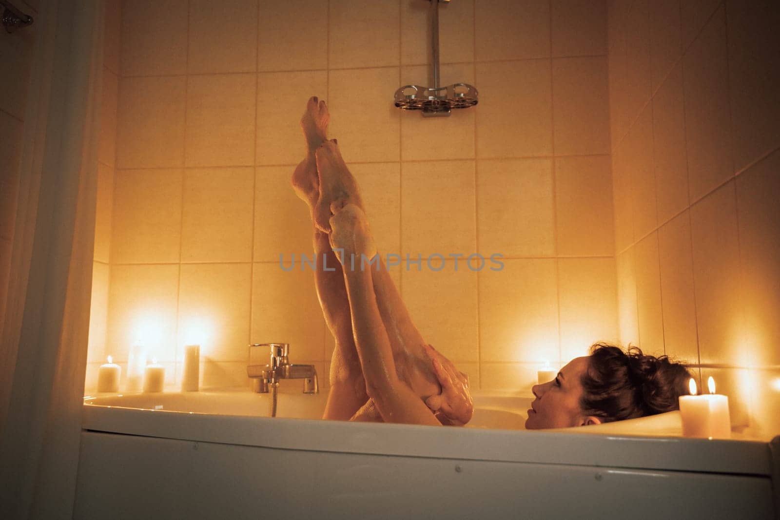 A woman is in a bathtub with candles lit around her. She is barefoot and has her legs up in the air