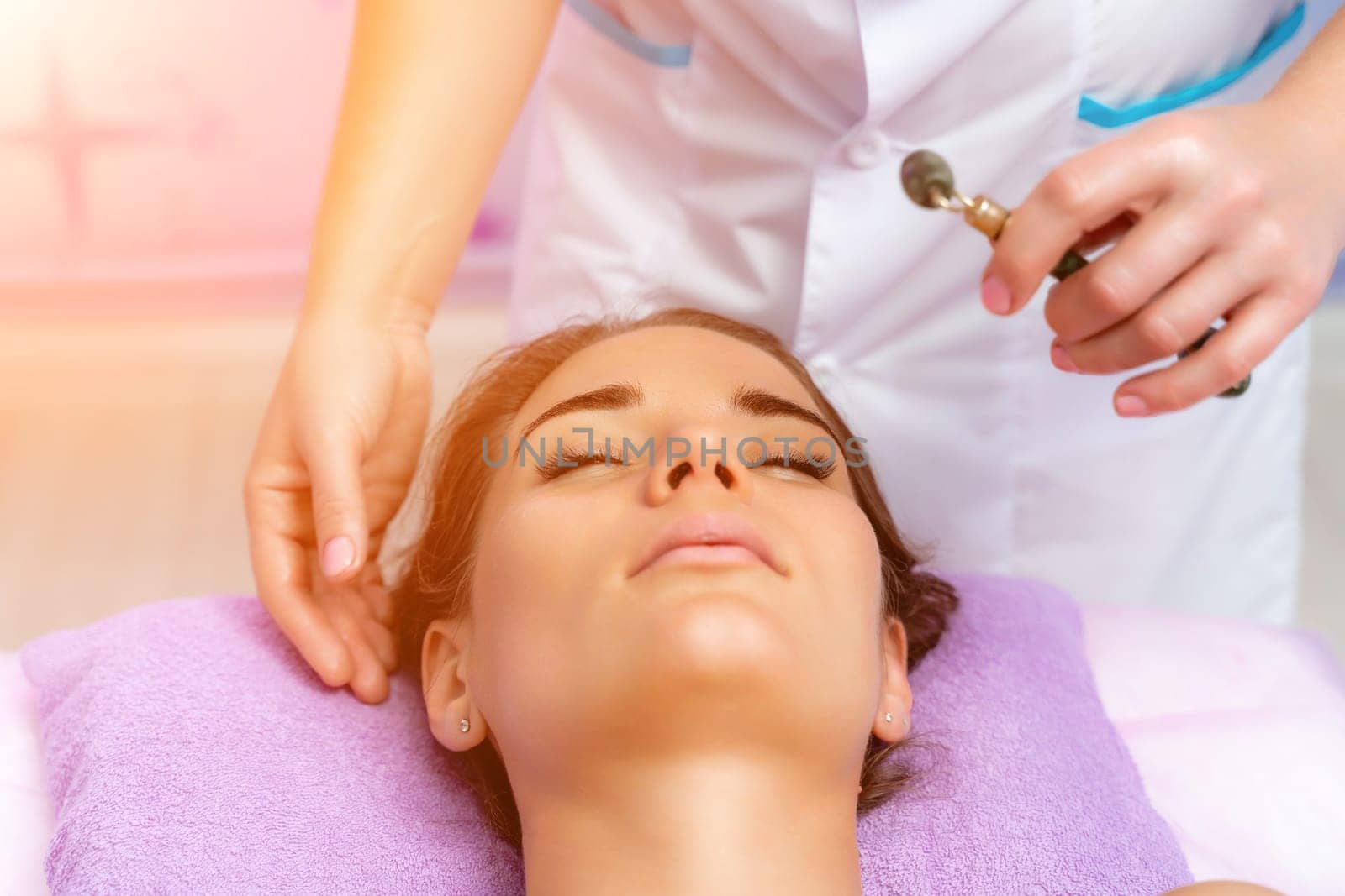 Facial massage. Side view european woman getting massage with jade face roller gouache in spa salon.