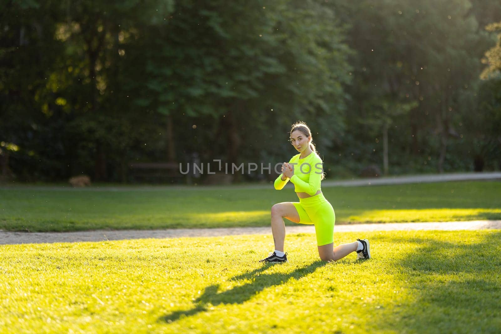 A woman in a neon green outfit is doing a yoga pose on a grassy field. The bright colors of her outfit and the lush green grass create a cheerful and energetic atmosphere