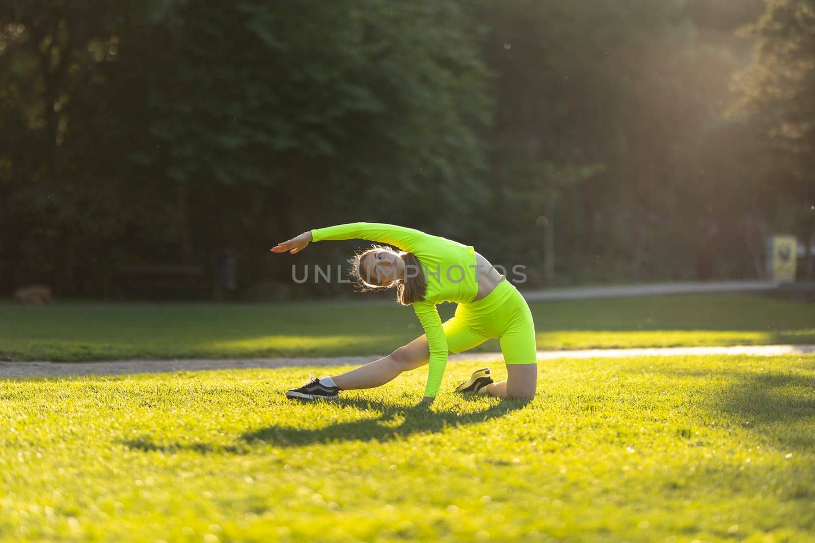 A woman in a neon green outfit is doing a yoga pose on a grassy field. The bright colors of her outfit and the surrounding green grass create a cheerful and energetic mood