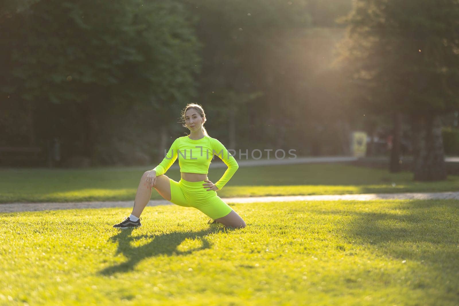 A woman in a neon yellow outfit is doing a yoga pose on a grassy field by Studia72