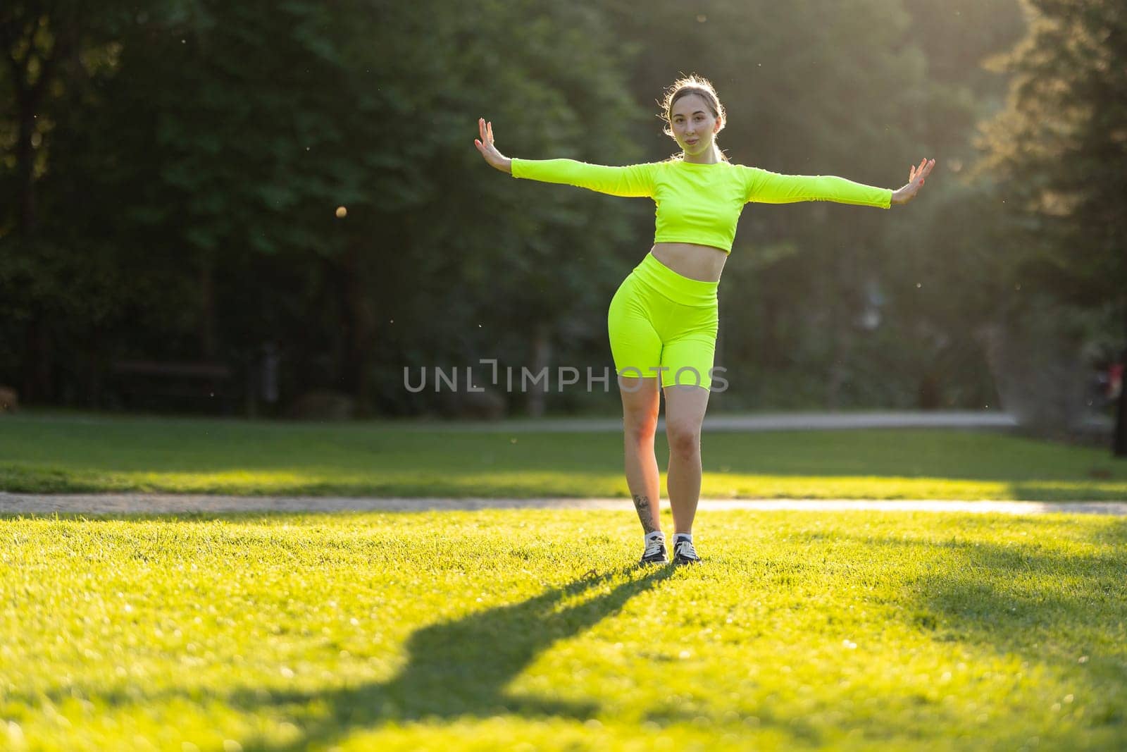 A woman in neon green is standing in a field of grass. She is wearing a neon green top and shorts