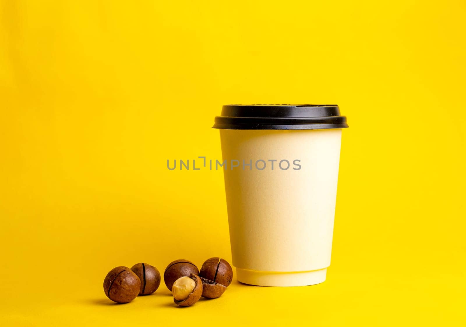 a glass of coffee with macadamia nuts on a yellow background.