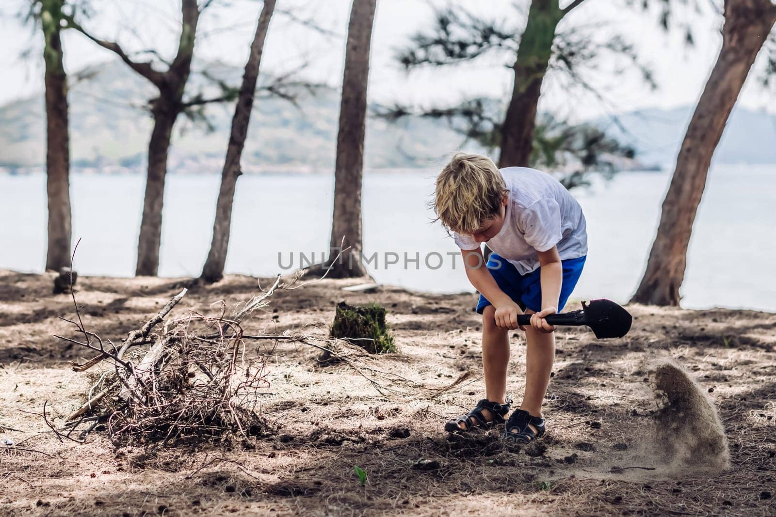 Cute boy digging soil in forest near sea beach. Family natural education skills. Travelling together. Learning camping organizing bonfire by nandrey85