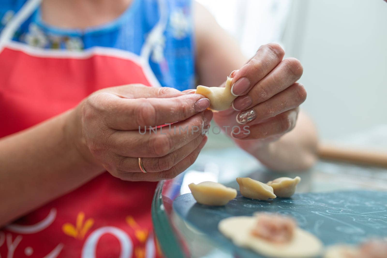 a woman in the kitchen prepares dumplings from dough and minced meat.