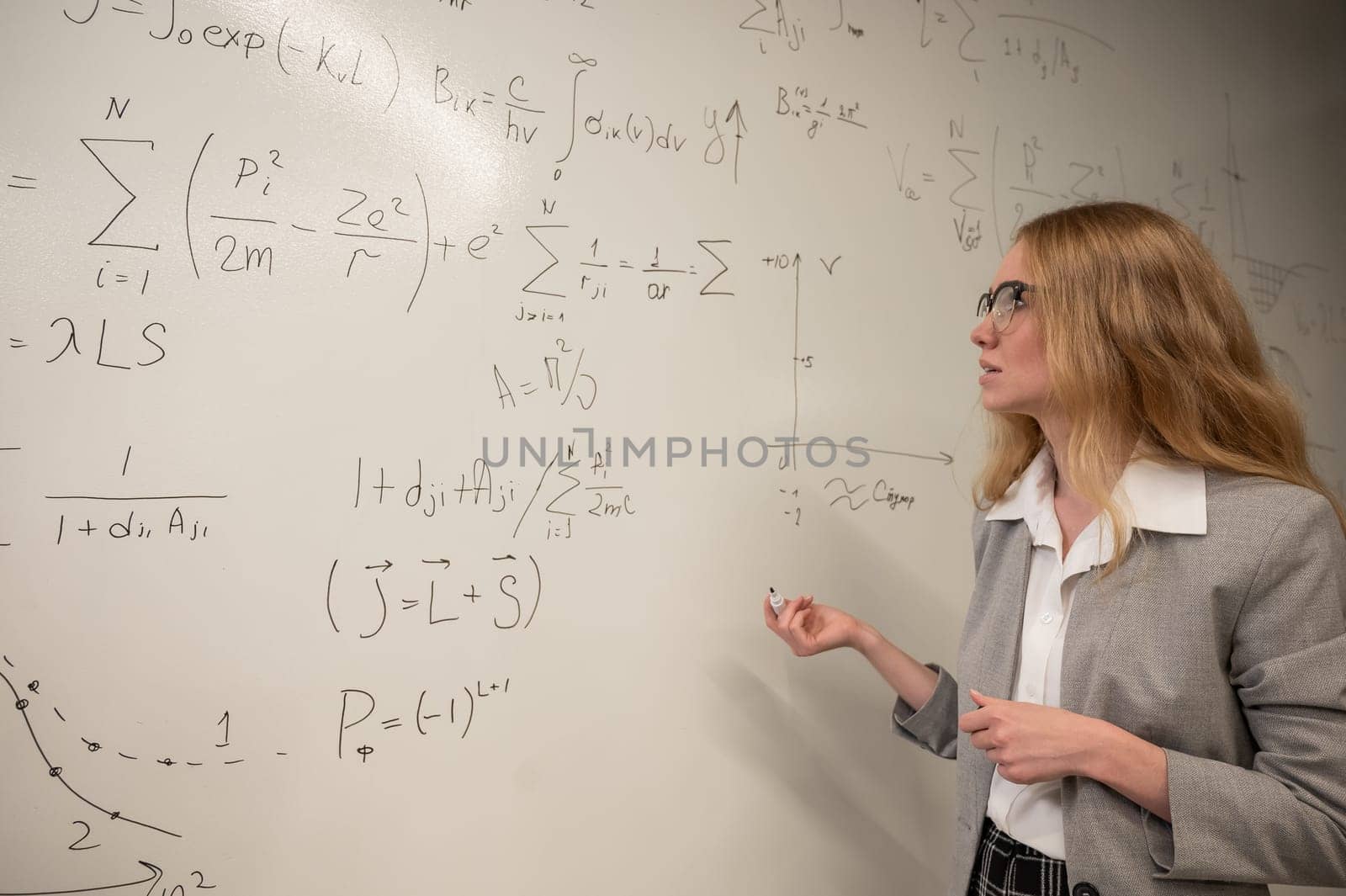 Young woman scientist writes formulas on a white board