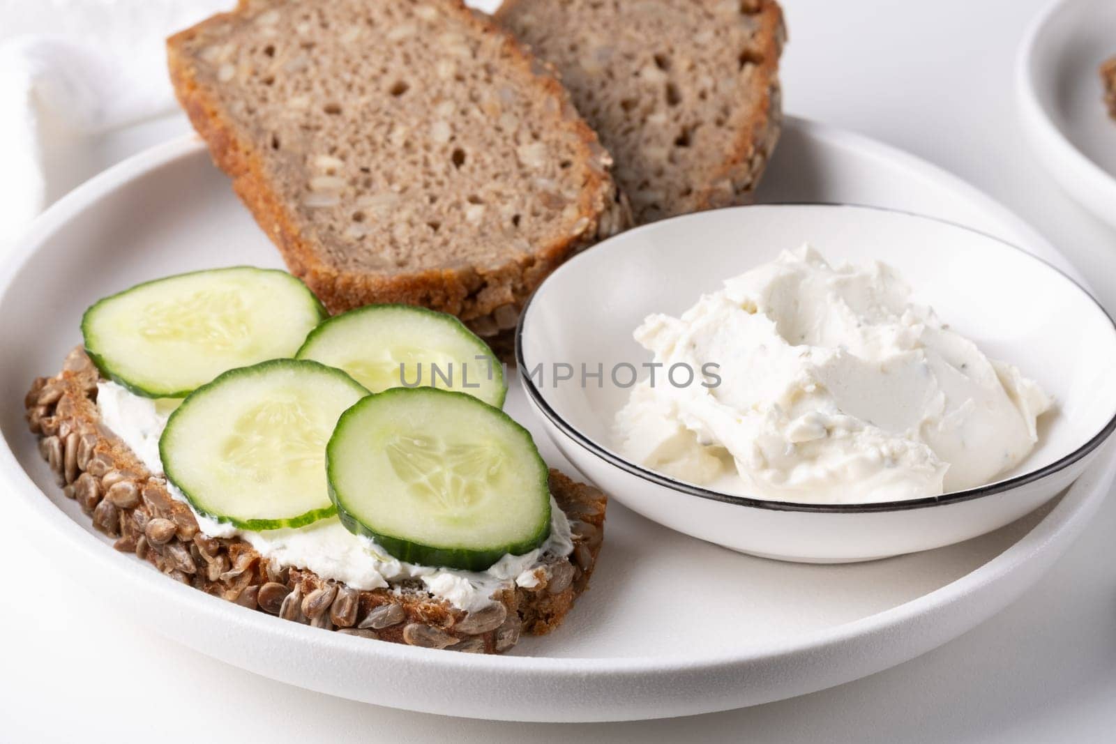 Rye bread with cream cheese and cucumbers on a white table by NataliPopova