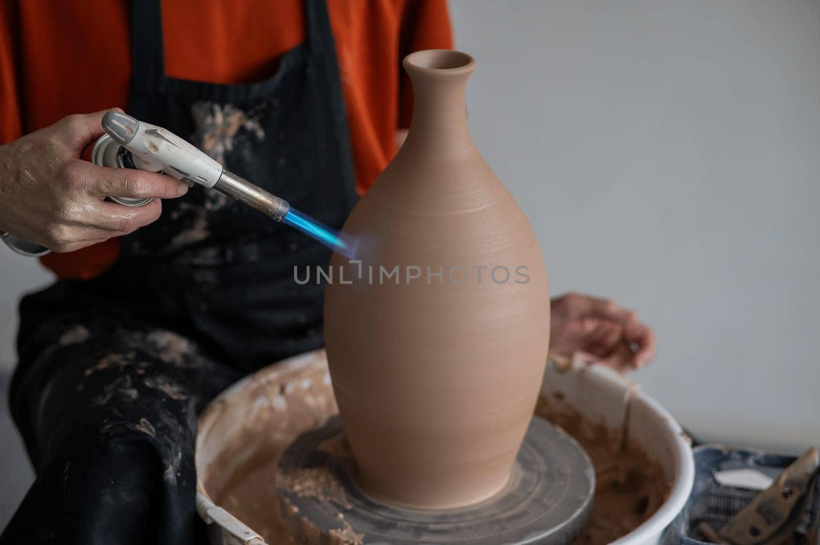 Close-up of a potter's hands firing a jug with a gas burner on a potter's wheel