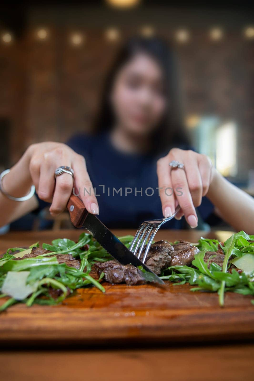 Girl eats steak with greens on a wooden board