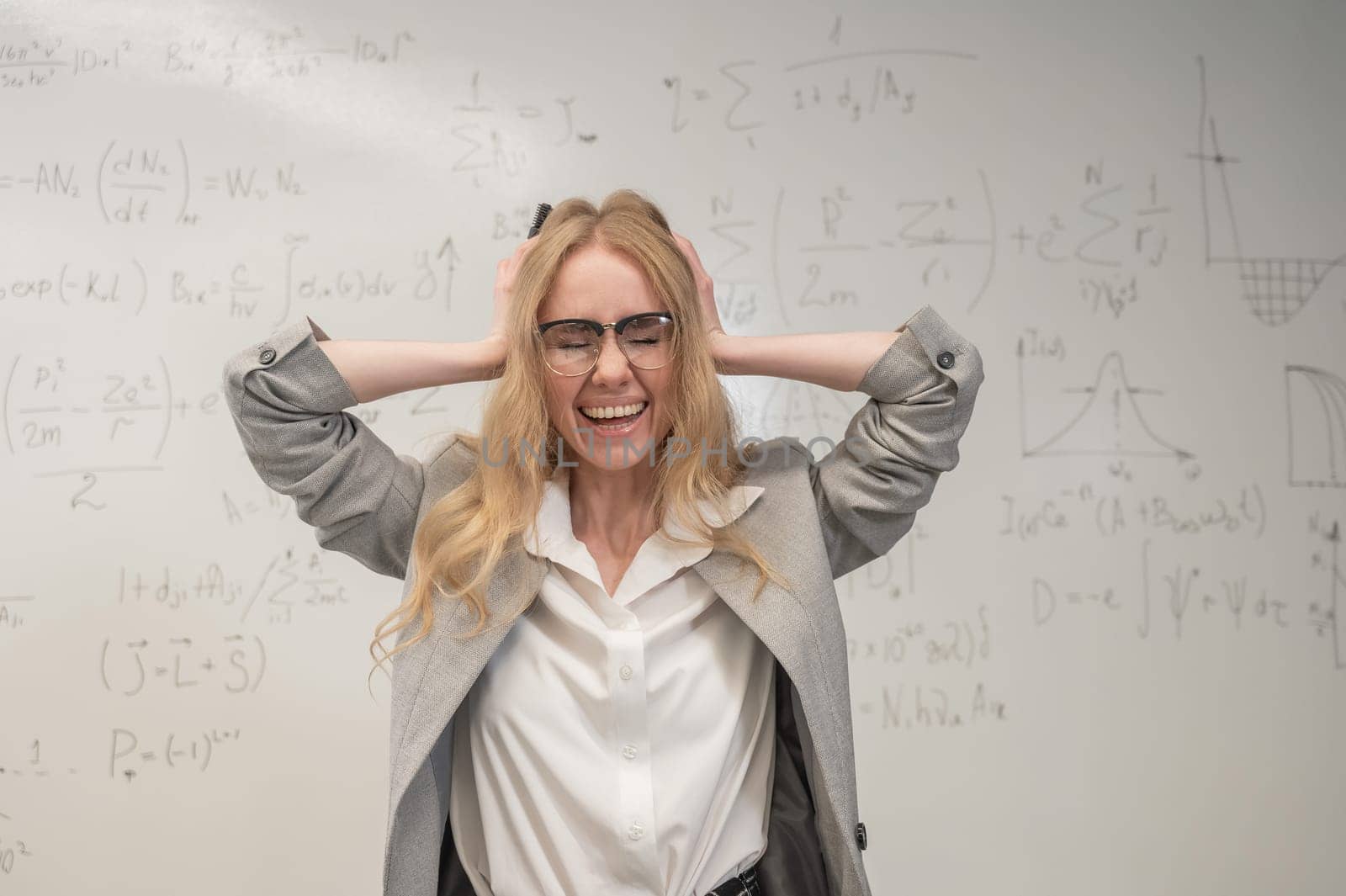 Caucasian woman stands by a white board and holds her head