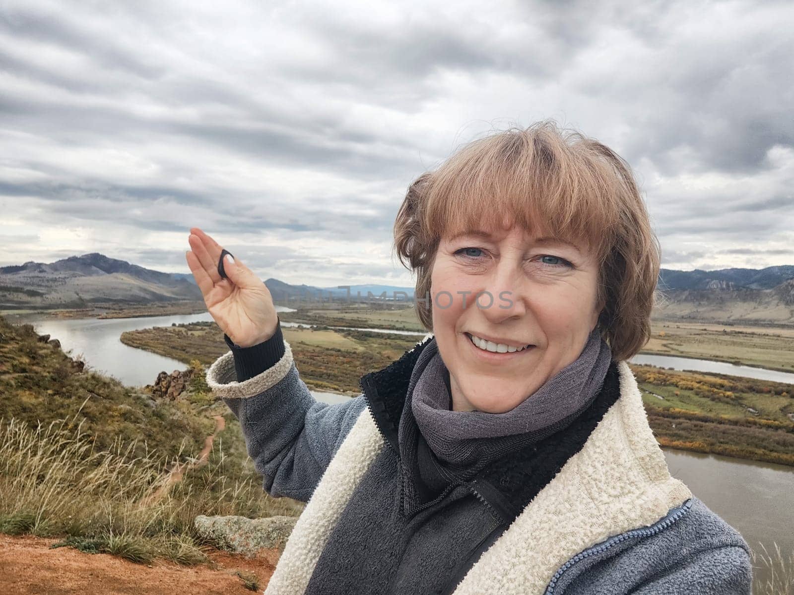 Happy female blonde tourist taking selfie picture with smart mobile phone outside. Middle aged woman having fun on adventure nature trip in mountain