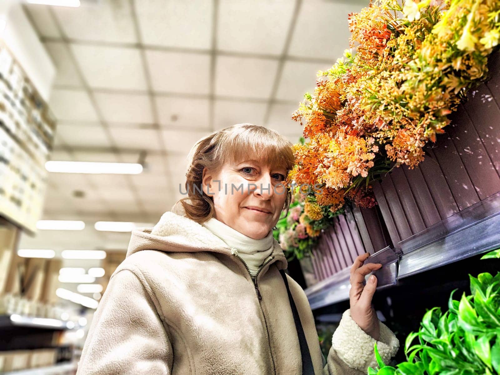 Portrait of girl with flowers on the shelves in the store. Middle-aged woman chooses flowers for planting. Woman Selecting Flowers at Garden Center