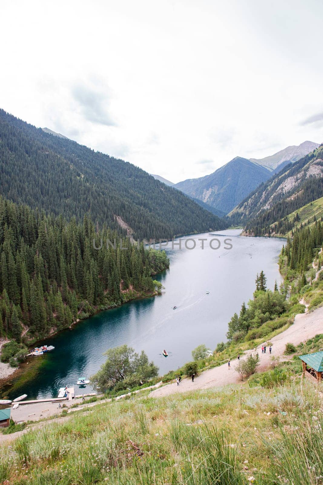 The lake is surrounded by green hills and the water is crystal clear. There is a building on the hill and trees on the shore.