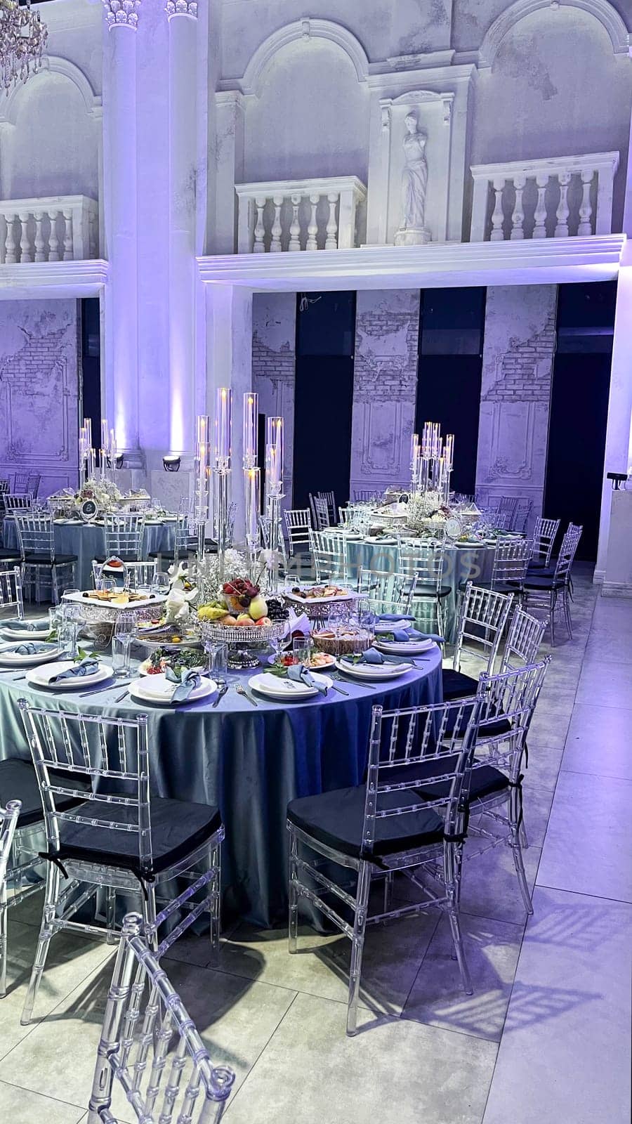 A large, elegant wedding reception hall with round tables, crystal chandeliers, and a balcony overlooking the dance floor.