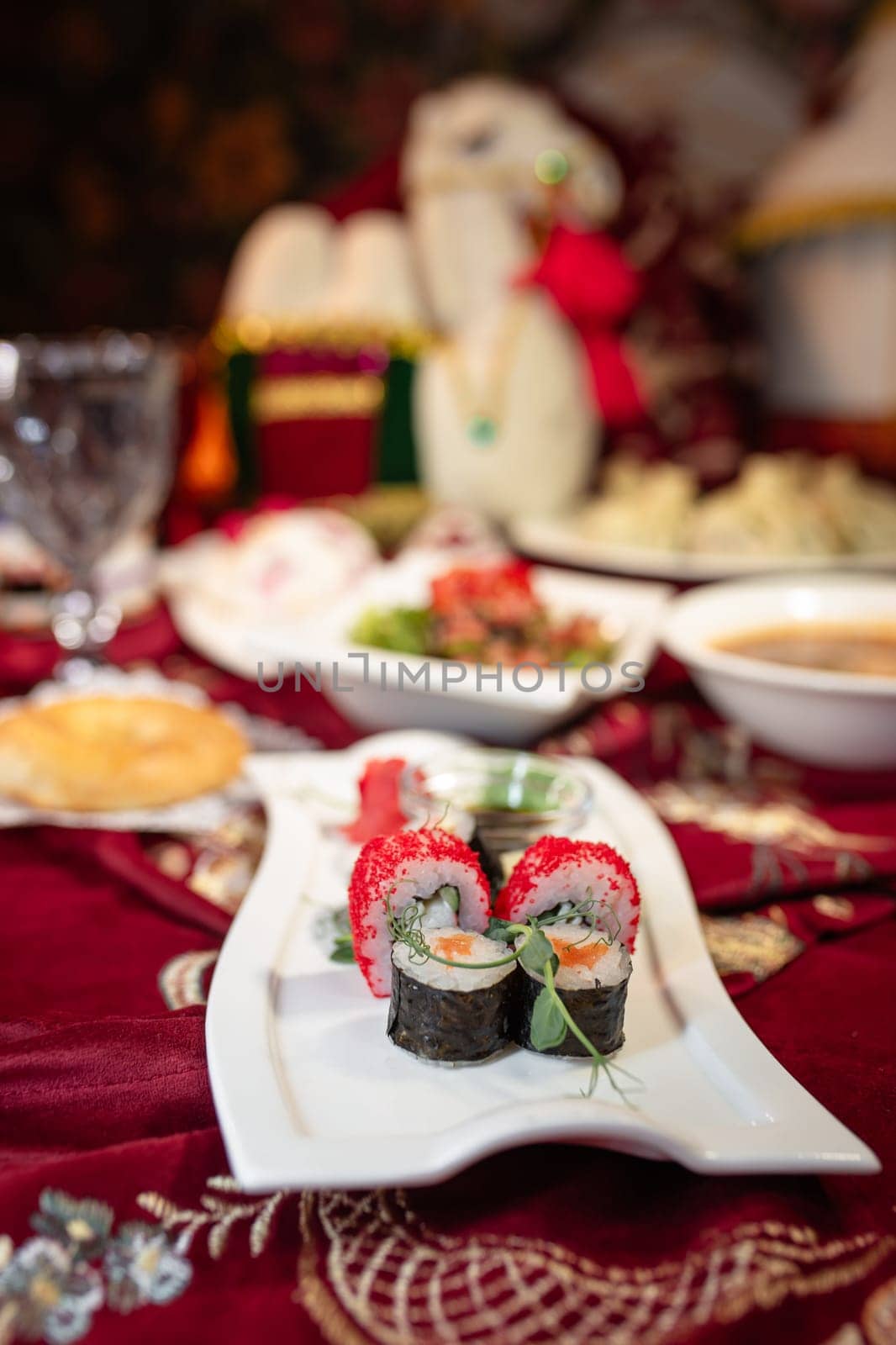 A variety of sushi rolls, along with other assorted dishes, are arranged on a table with a red tablecloth.