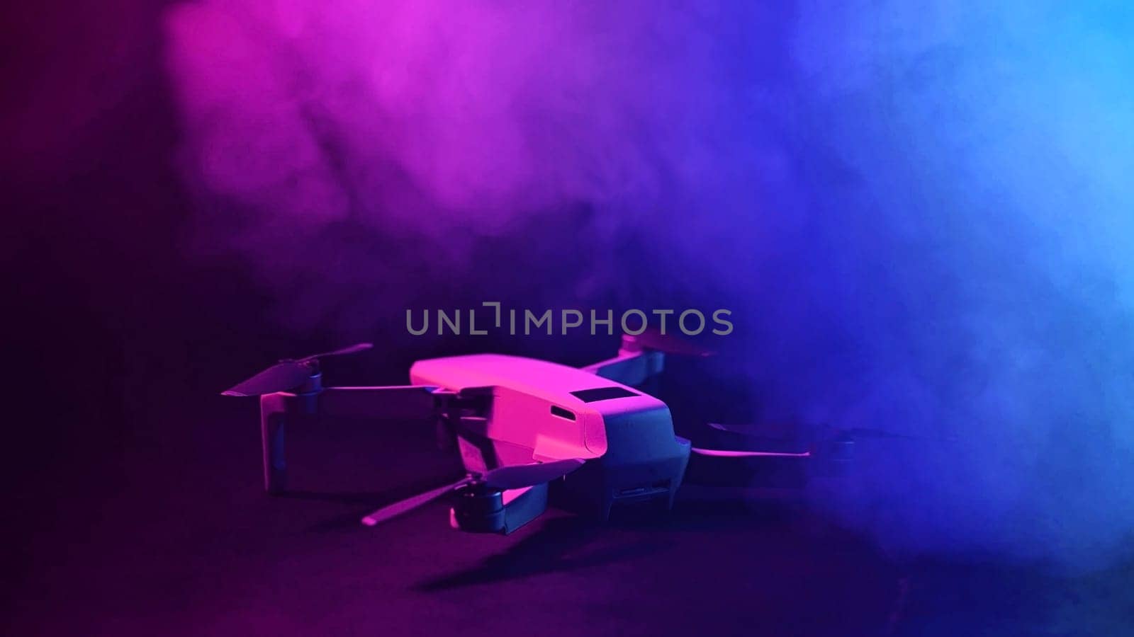 Quadrocopter in clouds of colored pink-blue smoke on a black background. by mrwed54