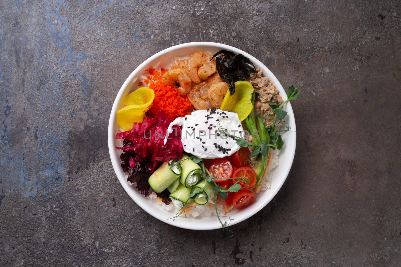 Scrumptious seafood rice bowl with fresh vegetables and egg on a dark background top view by Pukhovskiy