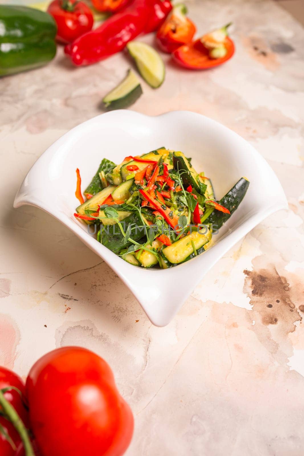 Fresh cucumbers, bell peppers, and herbs on white plate, pink background by Pukhovskiy