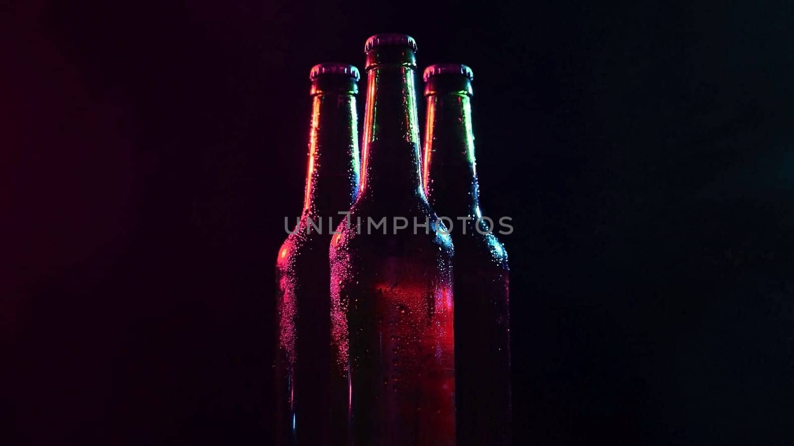 Three bottles of beer spinning in colored light on a black background