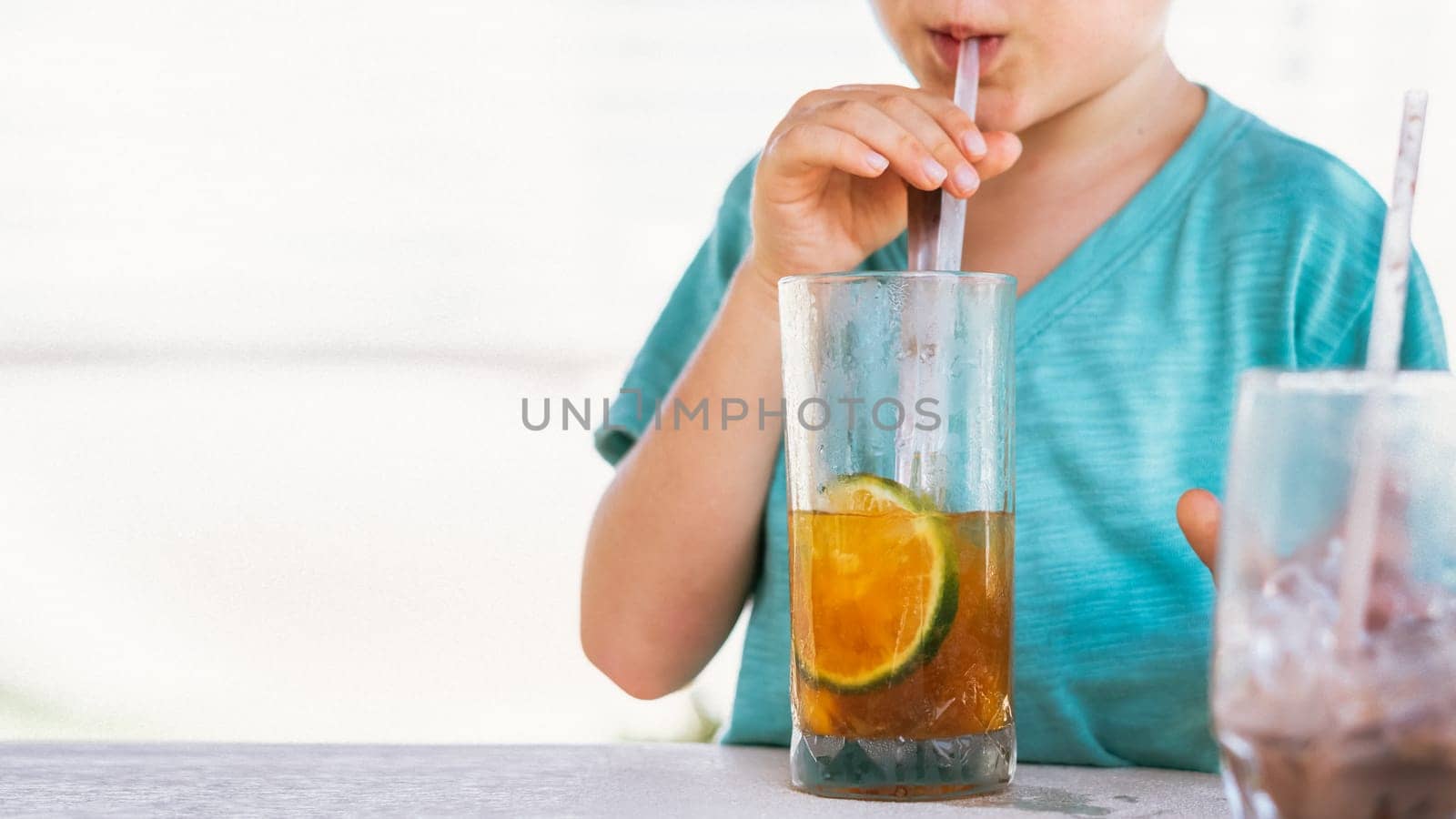 Happy childhood. Boy drinking fruit tea with ice in hot summer day time. Cute lover of sweets and tasty things.