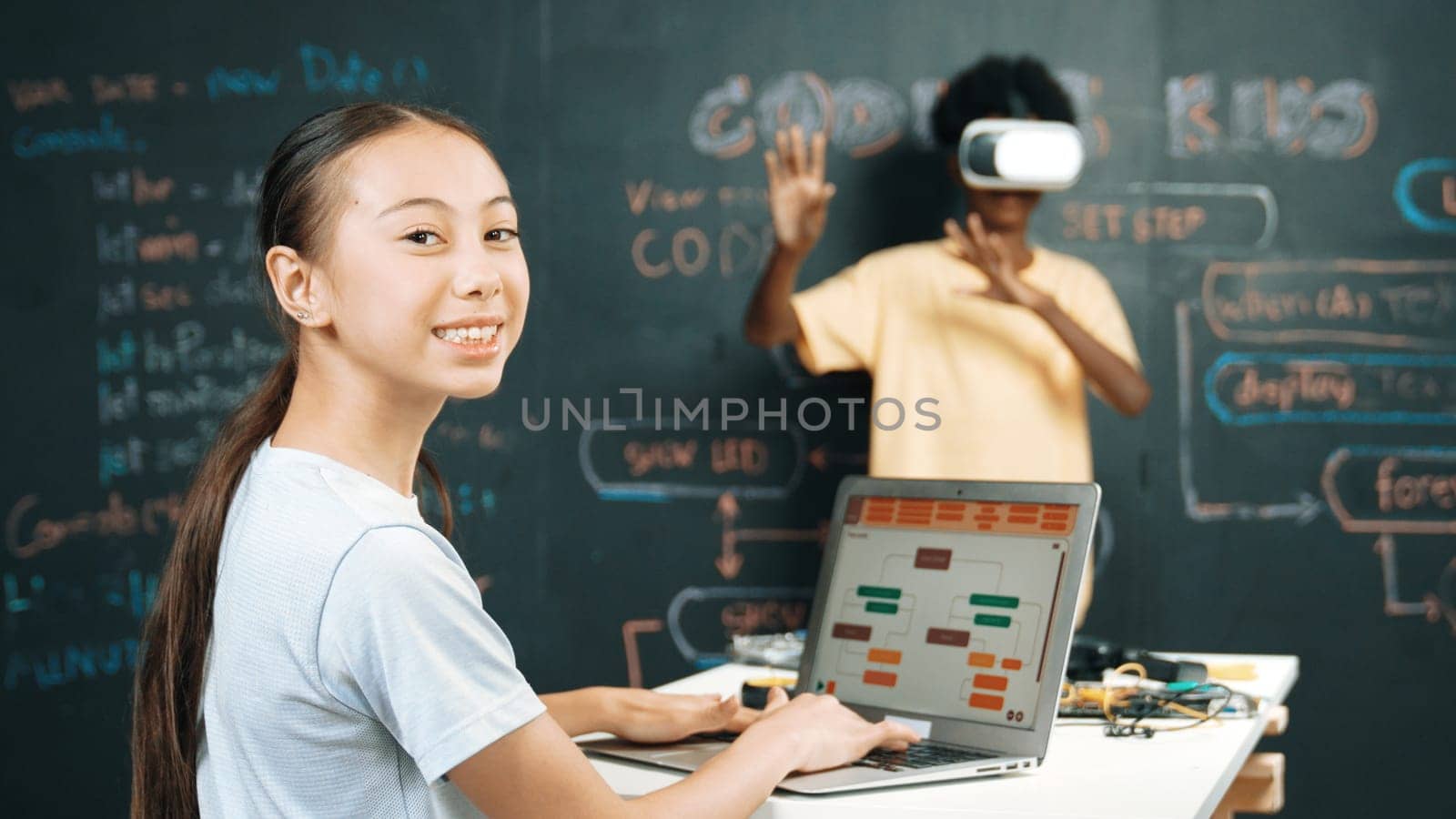 African boy using VR glasses while young woman looking at camera and coding or programing system. Smart teenager standing at blackboard while touching in simulate program at STEM class. Edification.